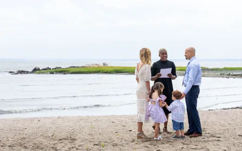 A couple stands on a beach with their two small children as the officiant reads the ceremony
