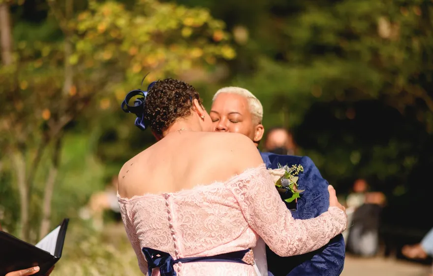 A couple hugs and kisses mid-ceremony while the officiant beside them keeps a black binder open in her hand