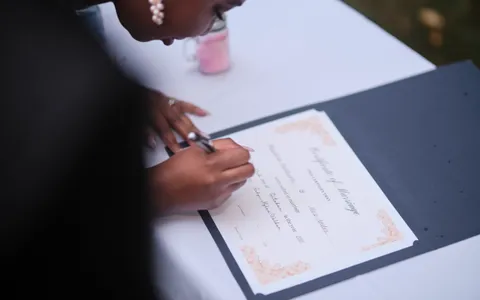 A hand signing a marriage certificate on a white tablecloth