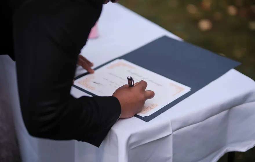 A hand signing a marriage certificate on a white tablecloth