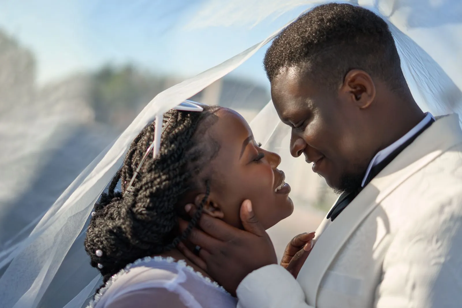 A smiling bride and groom face each other beneath the bride's flowing veil