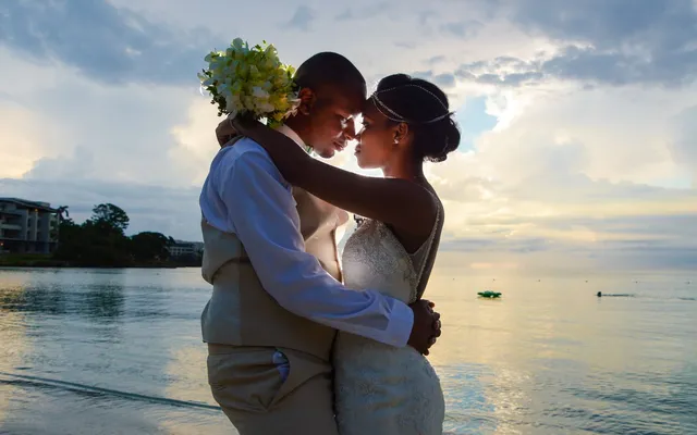 A bride and groom embrace forehead to forehead on a Caribbean beach at sunset