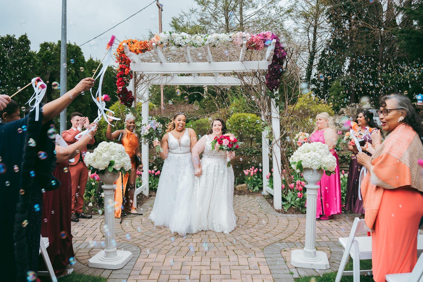 Two brides celebrating their recessional while guests blow bubbles over the aisle