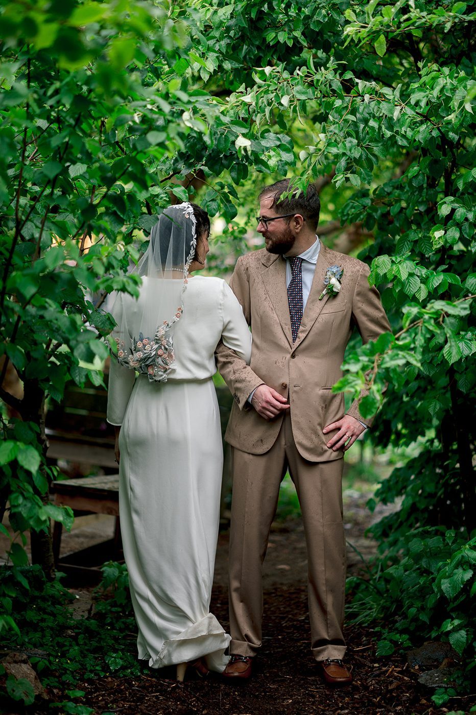A bride and groom pausing beneath green branches at an intimate NYC ceremony