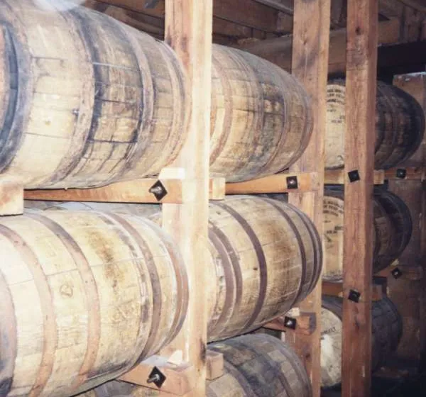 Rows of full-size oak whiskey barrels lying on their sides in wooden racks inside a dim aging warehouse