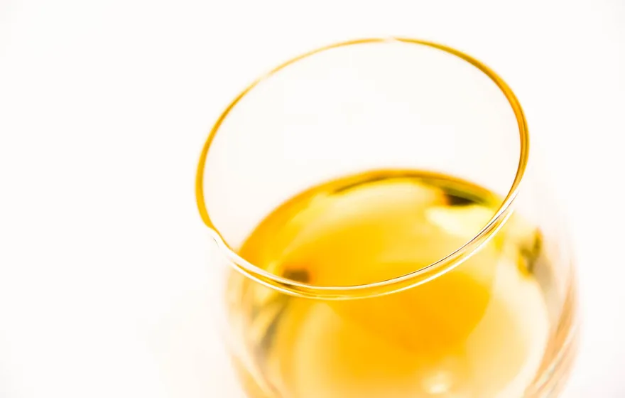 An overhead macro of a tasting glass holding a measure of bright amber whisky against a white background