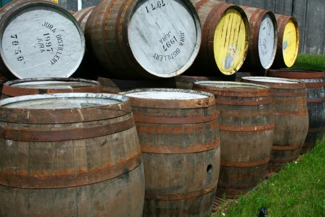Weathered oak whisky casks stacked outdoors at the Jura distillery, their heads dated 1997 and painted white and yellow