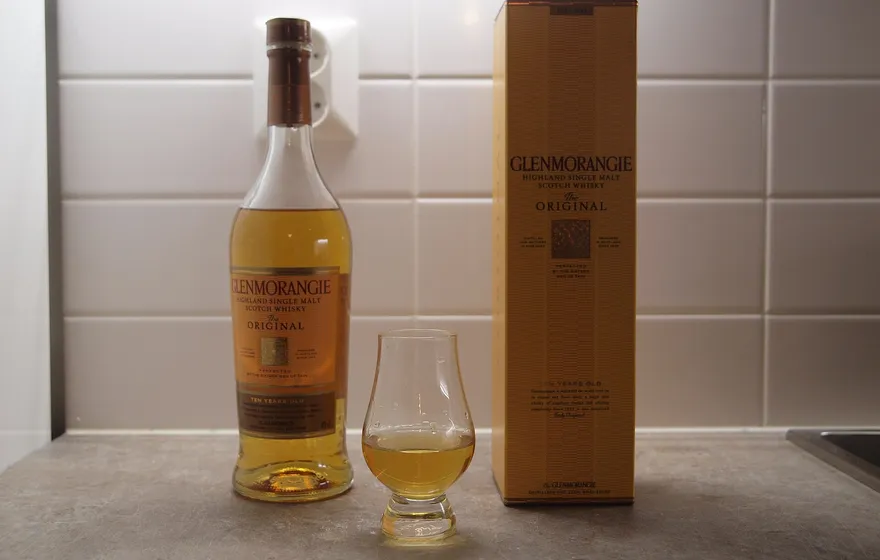 A bottle of Glenmorangie single malt Scotch whisky beside a small tasting glass holding a measure of amber spirit, with the gift box behind
