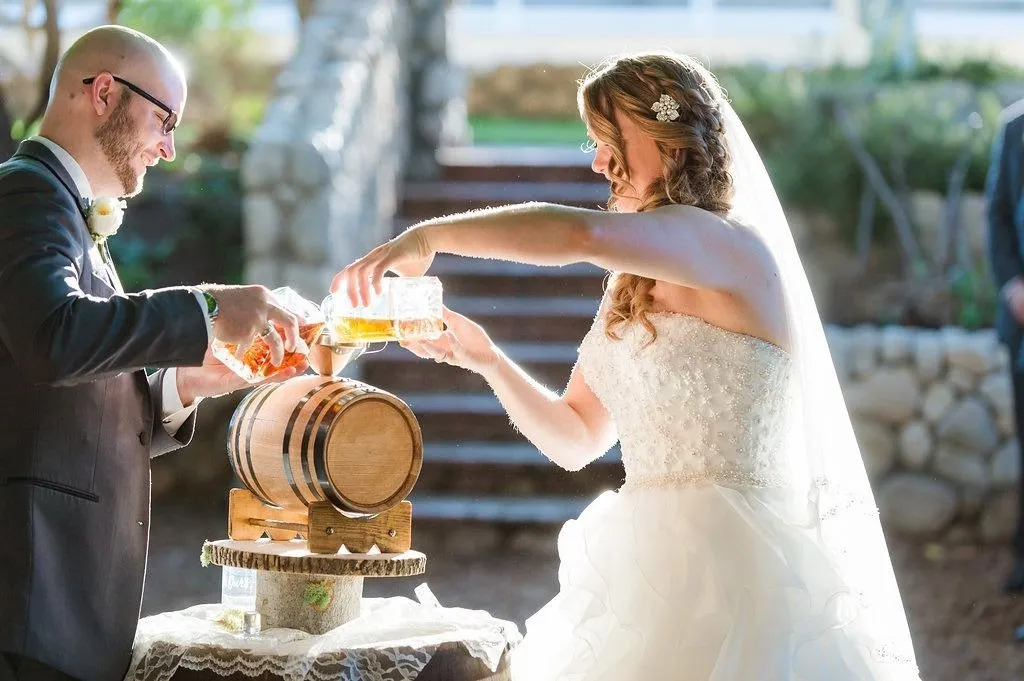 A couple pouring their separate spirits into a small oak barrel during a whiskey unity ceremony