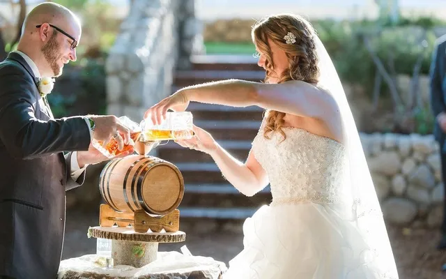 A couple pouring their separate spirits into a small oak barrel during a whiskey unity ceremony