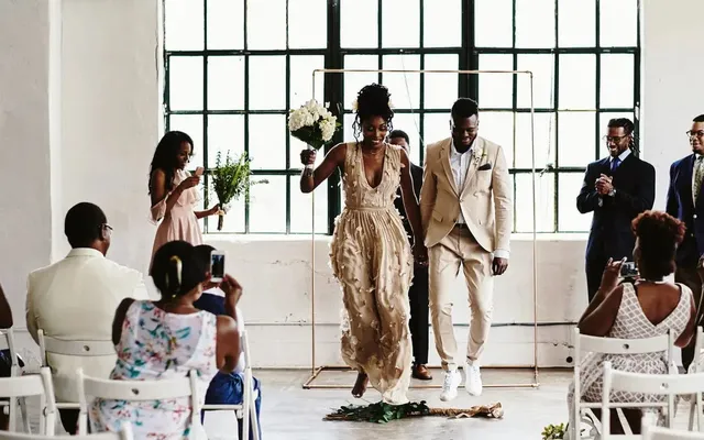 A couple jumping over a decorated broom at their wedding