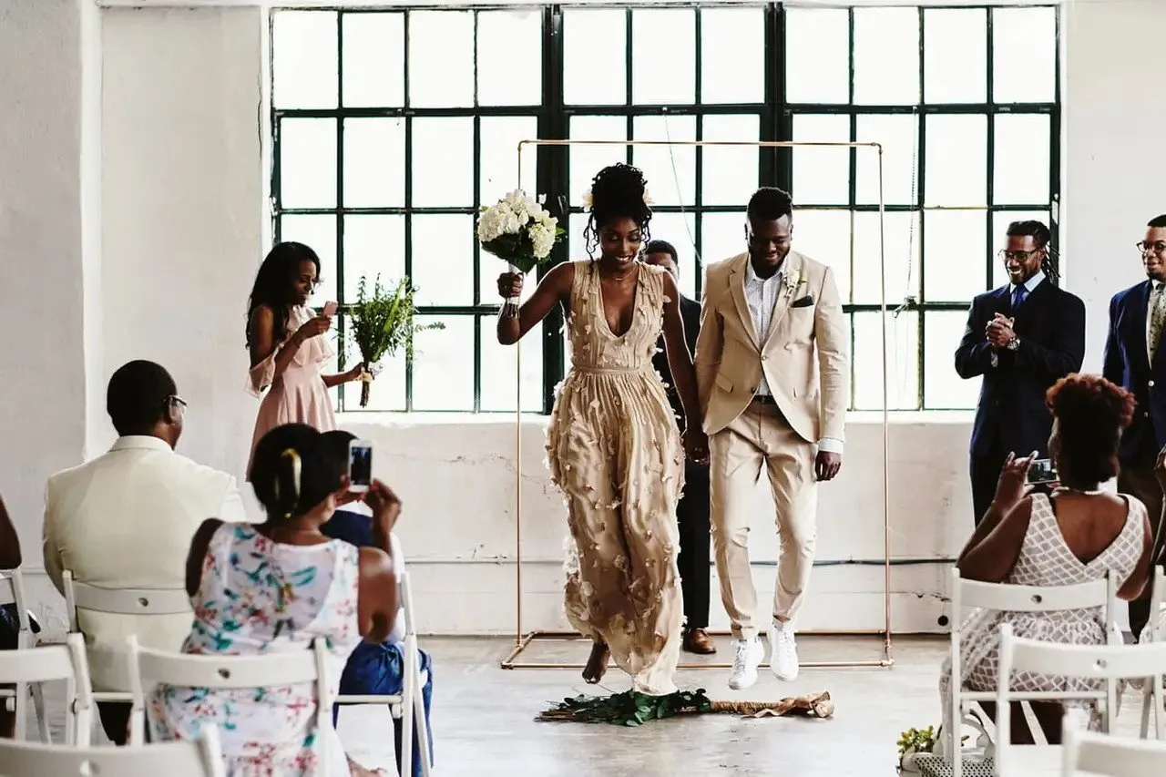 A couple jumping over a decorated broom at their wedding