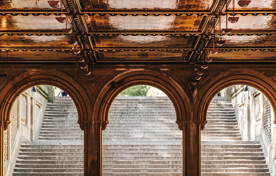 Looking out from under the arches of the Bethesda Terrace arcade toward the wide stone staircase, the tiled ceiling overhead
