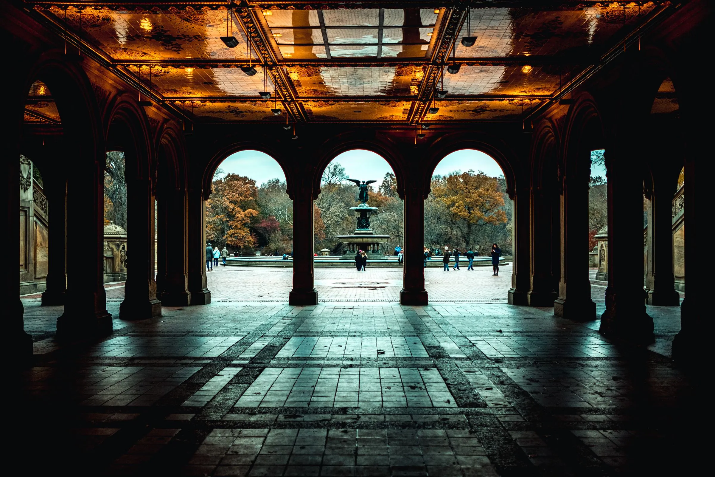 The arcade beneath Bethesda Terrace in Central Park, its tiled ceiling lit warm, with Bethesda Fountain framed in the center arch