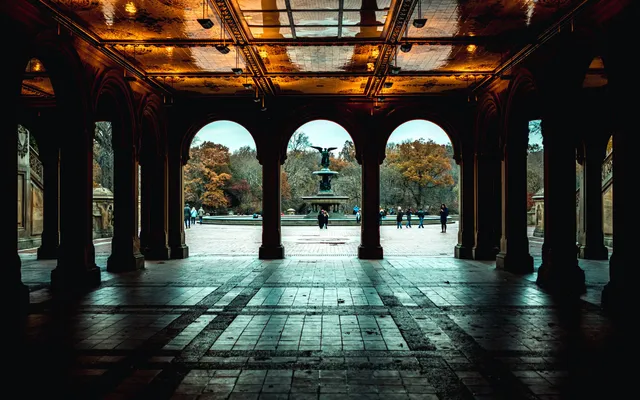 The arcade beneath Bethesda Terrace in Central Park, its tiled ceiling lit warm, with Bethesda Fountain framed in the center arch