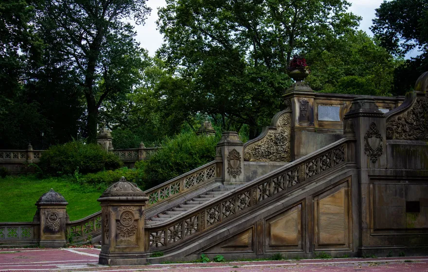 The carved sandstone staircase and balustrades of Bethesda Terrace rising from the brick plaza, with trees behind