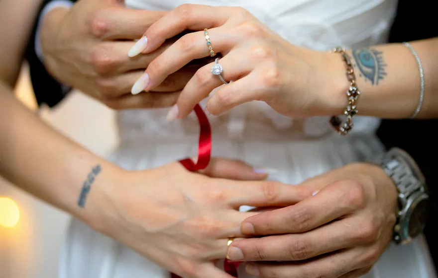 Close-up of a bride and groom's hands joined at her waist, a thin red ribbon looped around their fingers