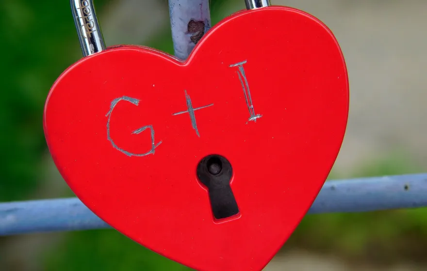A red heart-shaped padlock scratched with the initials G and I, locked onto a blue metal railing