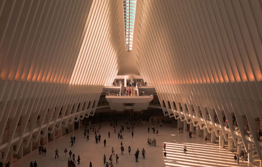 The white ribbed interior of the Oculus at the World Trade Center, warm light falling across the marble floor and the people crossing it