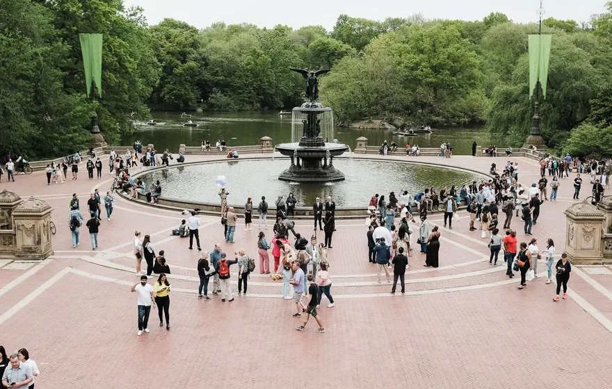 Bethesda Terrace seen from above, dozens of visitors spread across the red brick plaza around the fountain