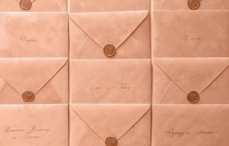 Rows of peach envelopes addressed in calligraphy and sealed with gold wax, laid out in a grid
