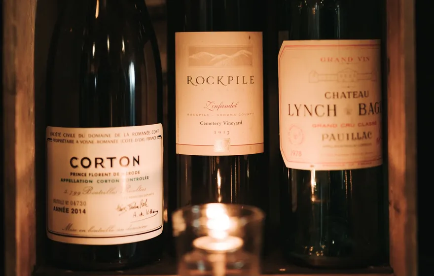 Three bottles of red wine standing in a rustic wooden crate, lit by a single candle