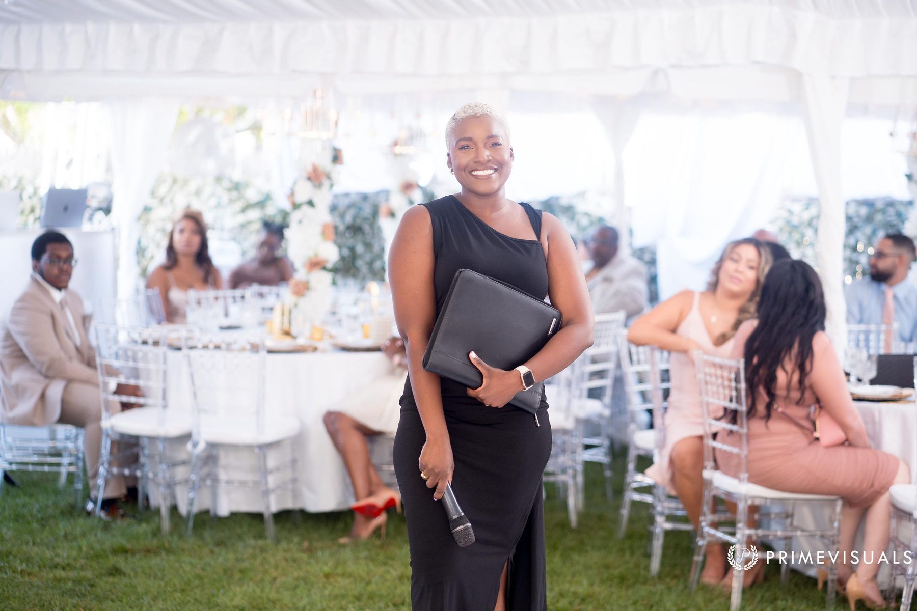 Robyn Walker smiling beneath a tented reception, ceremony folio and microphone in hand
