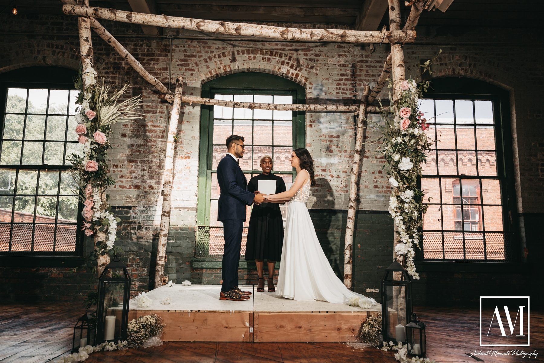 Robyn officiating a couple's vows beneath a birch arch at a Brooklyn warehouse wedding