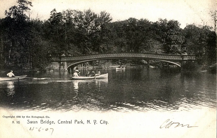A black-and-white early 1900s postcard of Bow Bridge over the Lake in Central Park, people in rowboats on the water, captioned Swan Bridge