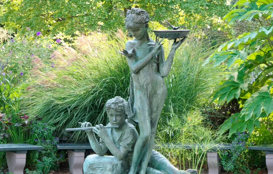 The bronze Burnett Fountain in the South Garden, a girl holding a bowl above a boy playing a flute, over a pool of water lilies
