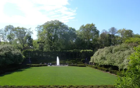 The Center Garden of Central Park's Conservatory Garden, a long lawn edged with hedges and flowering trees and a jet fountain at the far end