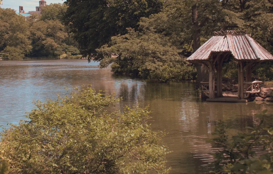 The rustic wooden shelter of Wagner Cove standing at the water's edge, seen across the Lake through green shrubs